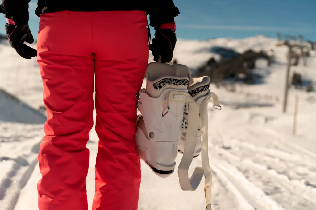 person-on-her-back-wearing-a-pink-ski-pant-holding-a-pair-of-ski-boots-in-a-ski-resort-in-the-alps.jpg